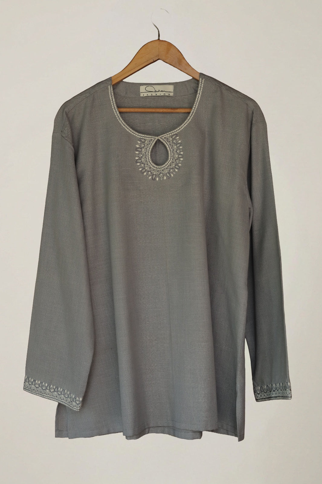 Gray long-sleeve top with embroidery on a wooden hanger against a plain background